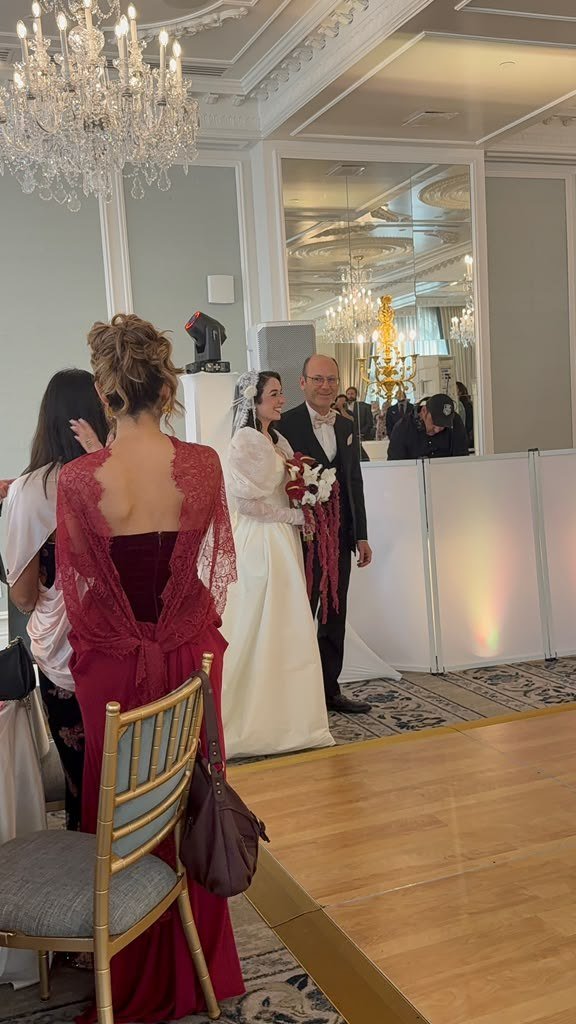 Laila and Chris greeting guests during their grand entrance under the crystal chandeliers at Hotel Carmichael, with the DJ booth and moving head lights visible in the mirrored ballroom